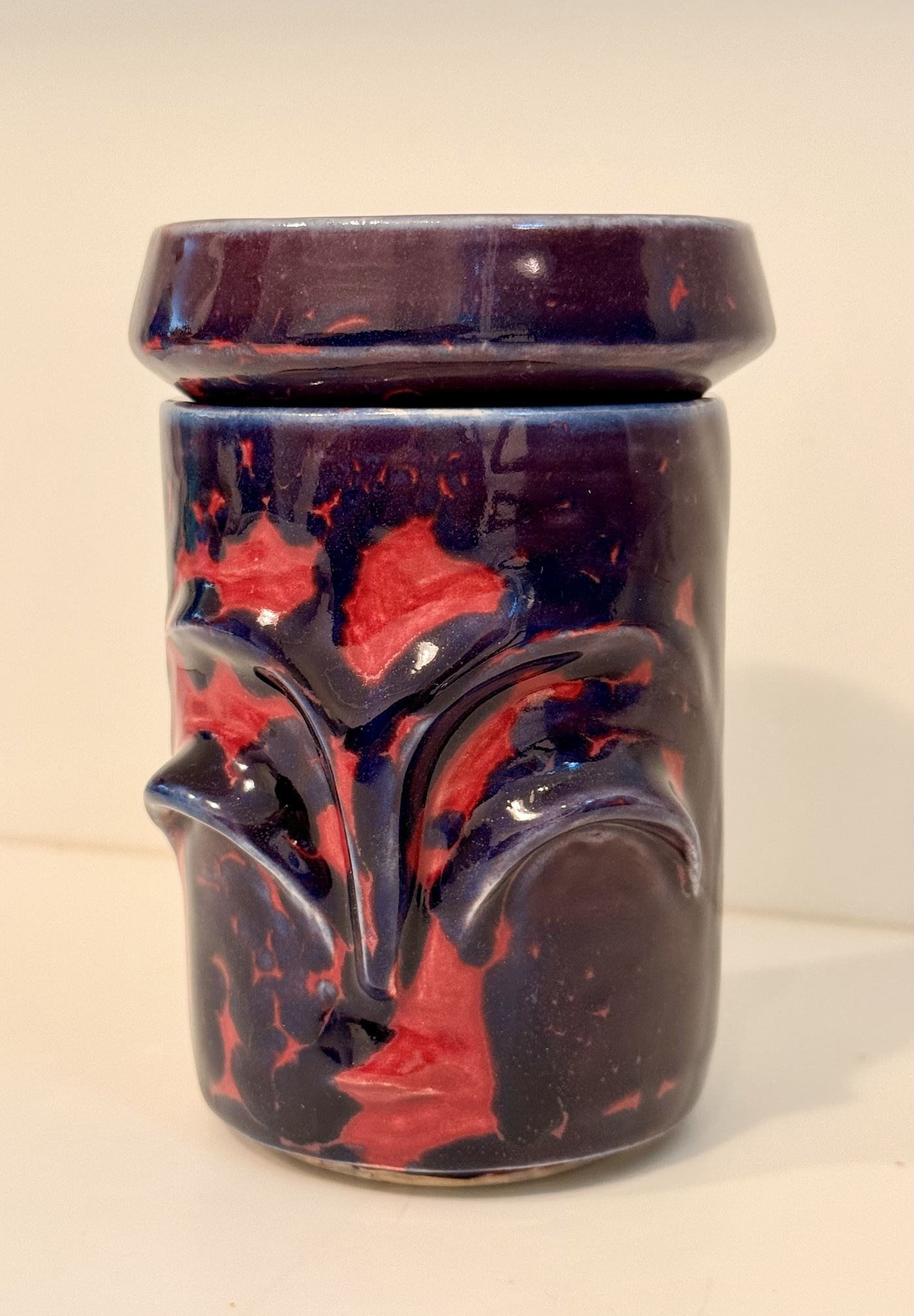 a red and purple ceramics jar with an abstract face on it